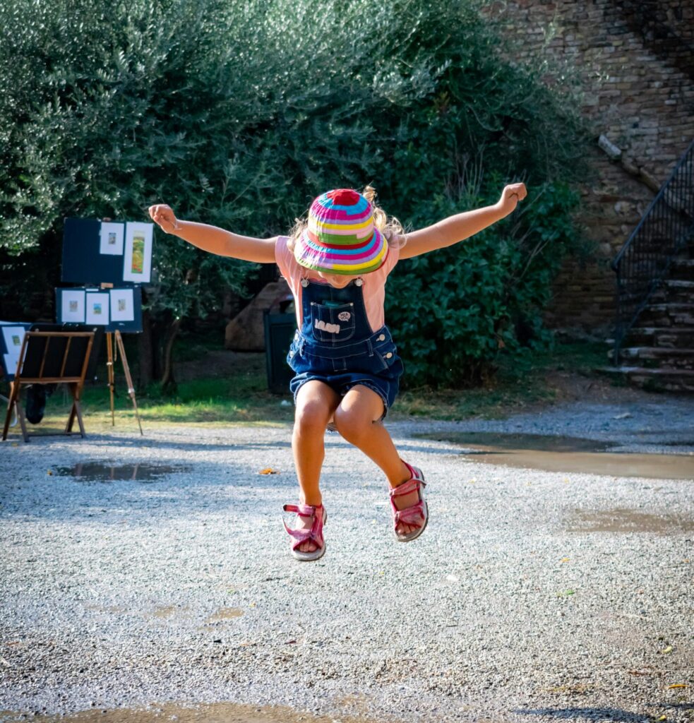 A vibrant scene of a child joyfully jumping in a park in San Gimignano, Italy, on a sunny day.