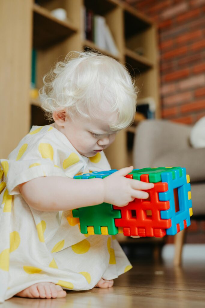 Charming toddler with light hair intently playing with vibrant building blocks on the floor indoors.
