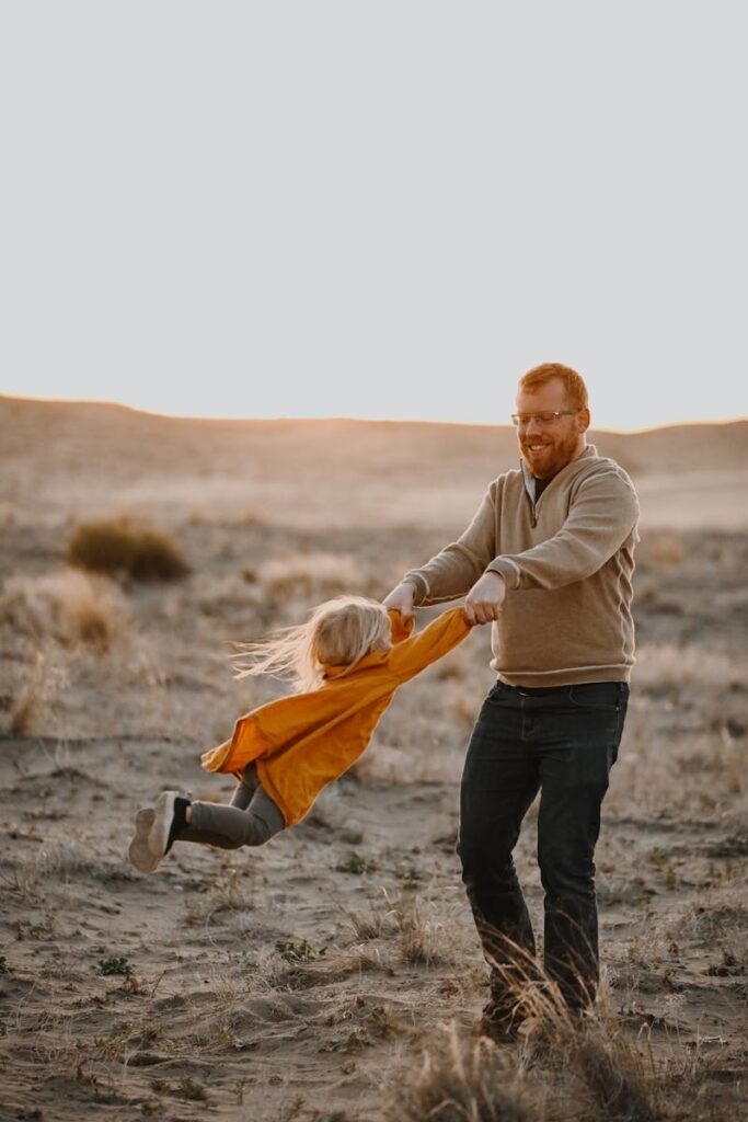A joyful father spins his daughter in a sunny desert landscape, capturing a playful and happy moment.