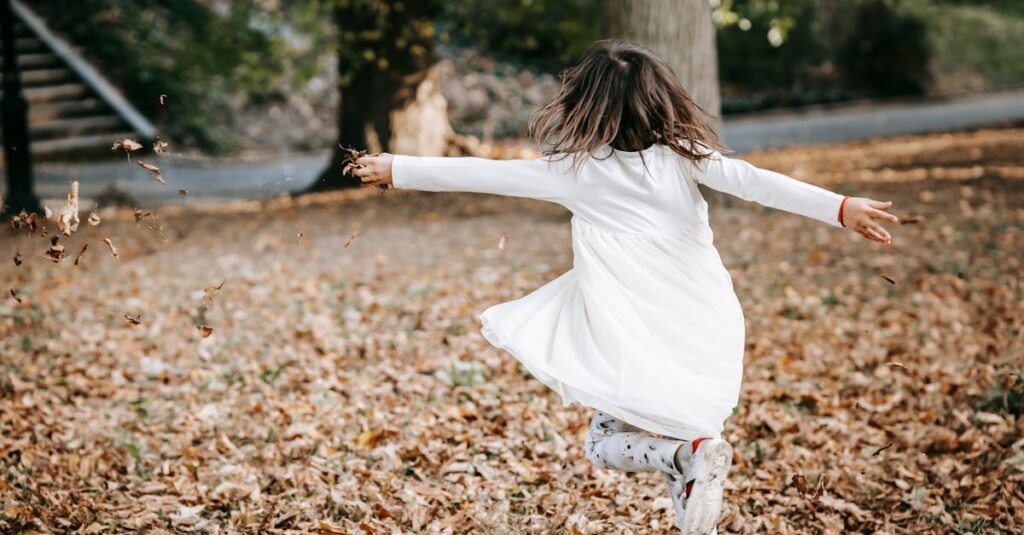 A young girl joyfully spins through fallen autumn leaves in a park, capturing the essence of carefree childhood.