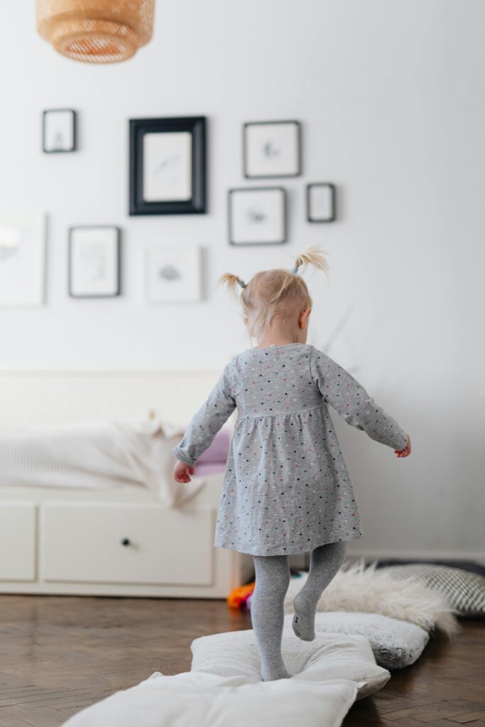 Young child joyfully playing indoors, jumping on cushions with a cozy atmosphere.