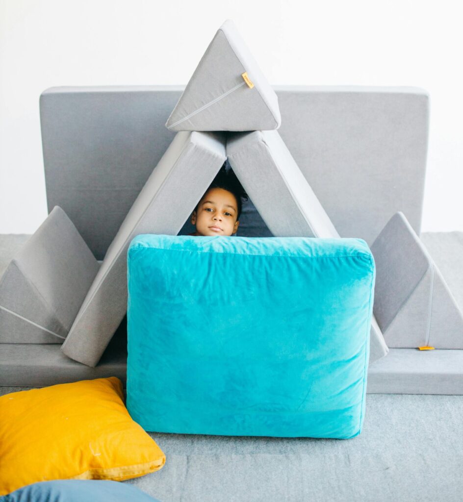 Cute child playing in a colorful cushion fort indoors, showcasing creativity and fun.