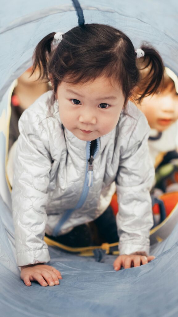 A young child with pigtails crawling through a play tunnel indoors.