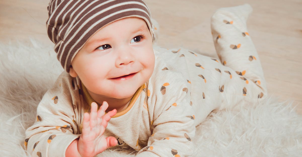 A cute baby in striped beanie lying on fluffy rug indoors, smiling with innocence.