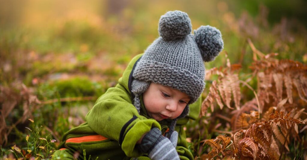 A cute baby in a knit hat and green outfit exploring nature during sunset.