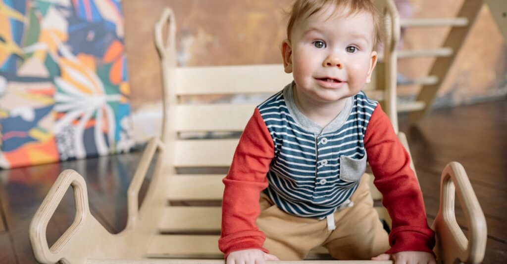 Cute toddler with blond hair plays indoors on a wooden toy, wearing colorful clothing, smiling at the camera.
