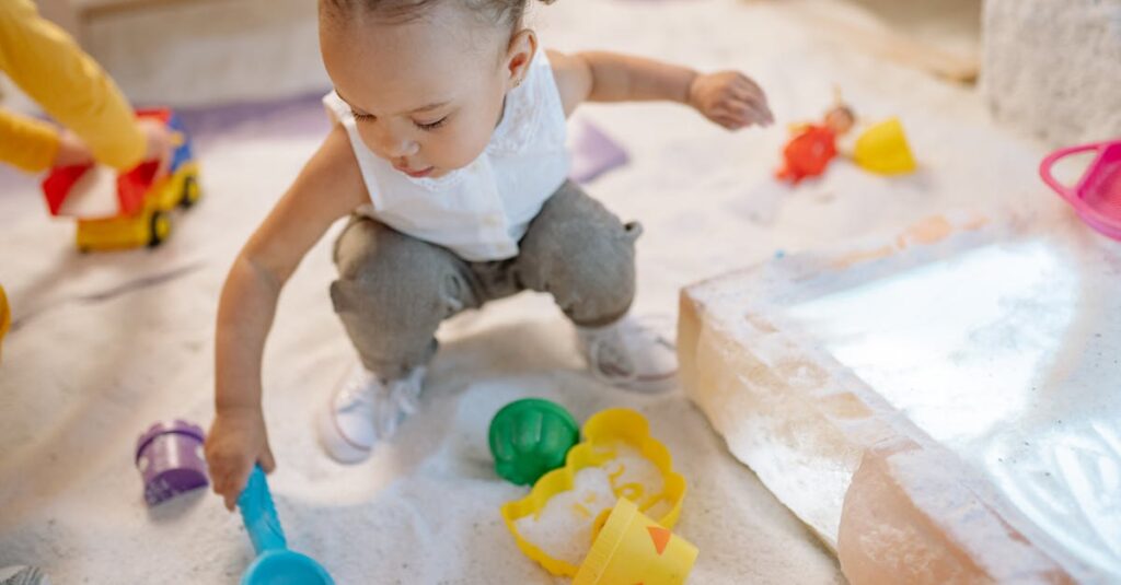 A toddler enjoys playing with colorful sand toys in an indoor play area, exploring and learning.
