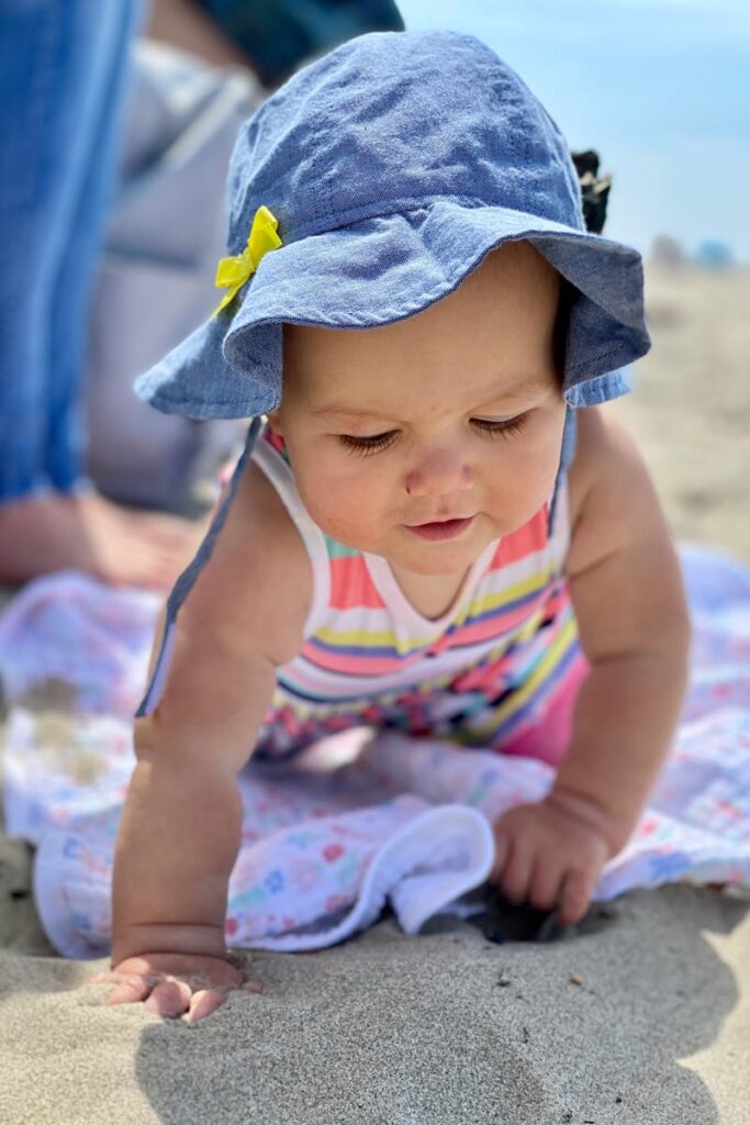 Charming baby crawling on Cannon Beach wearing a cute blue hat, perfect sunny day scene.