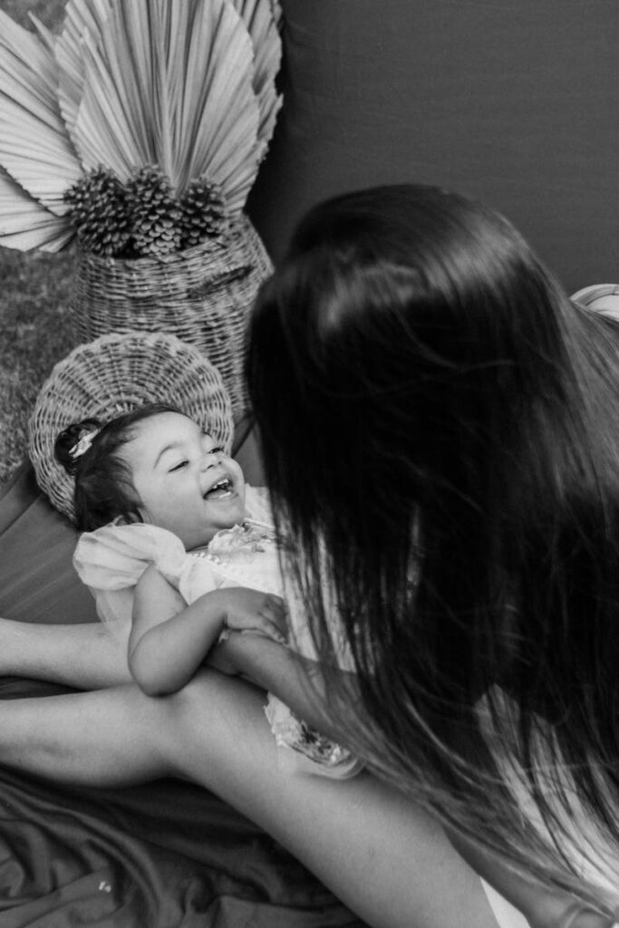 Tender black and white photo of a mother joyfully interacting with her child indoors.