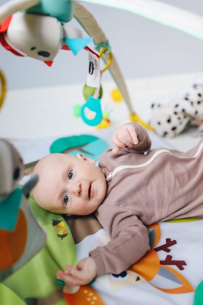 A cute baby lying on a colorful activity mat, engaging with soft toys overhead.