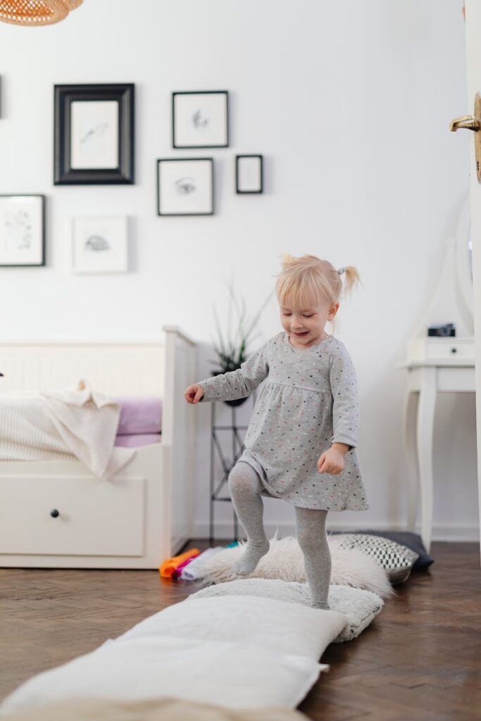 A playful toddler girl balancing on a soft cushion path in a cozy indoor setting.
