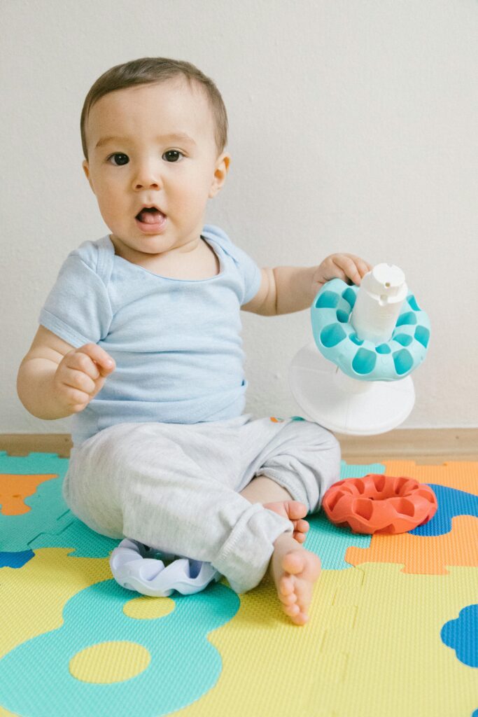Cute toddler in blue sitting on colorful puzzle mat playing with toys indoors.