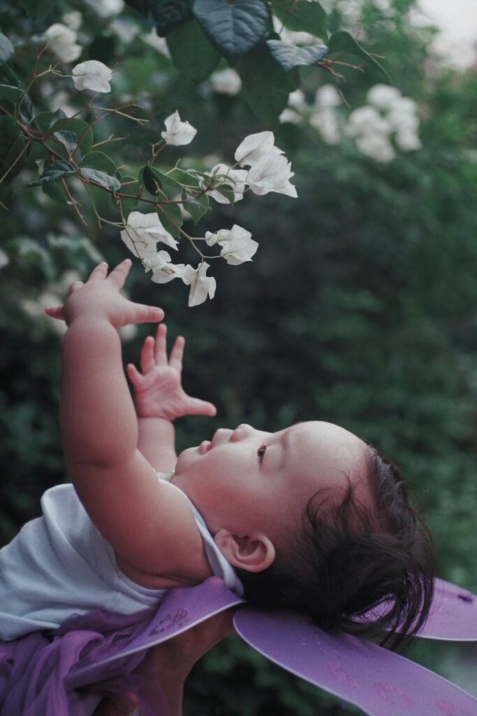 Adorable baby reaching for white bougainvillea flowers on a serene summer day.