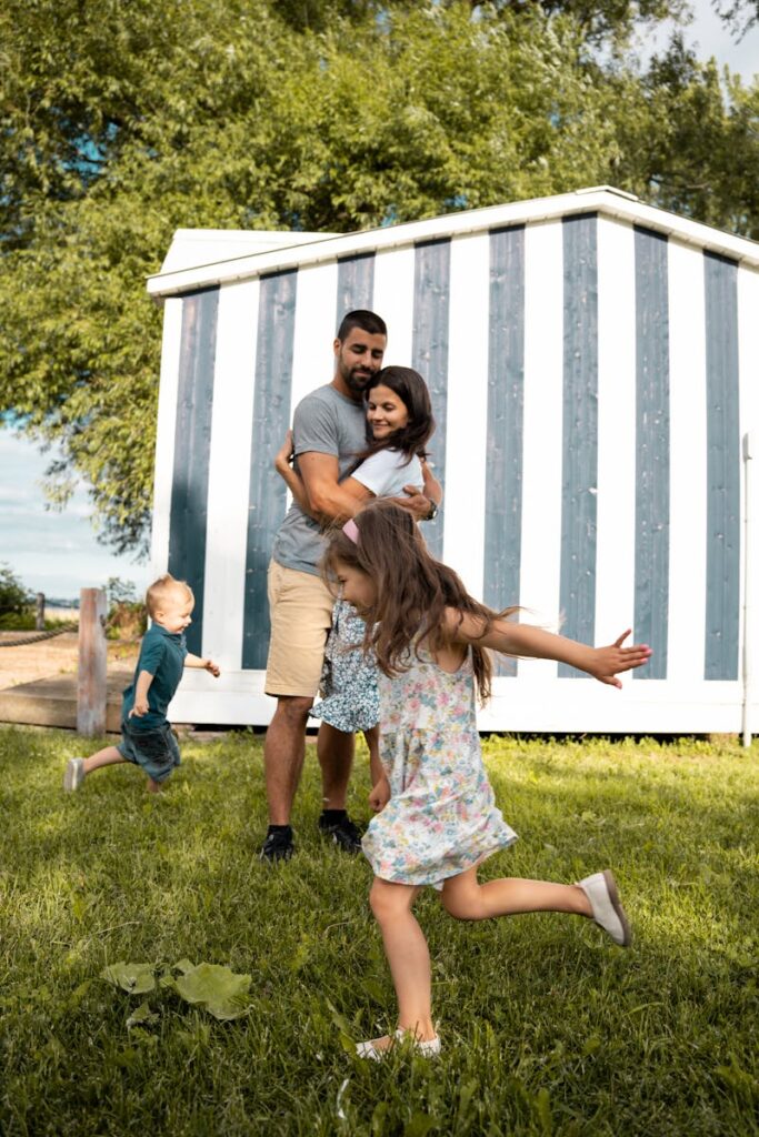 Family having fun outdoors with kids playing on grass against a striped shed.