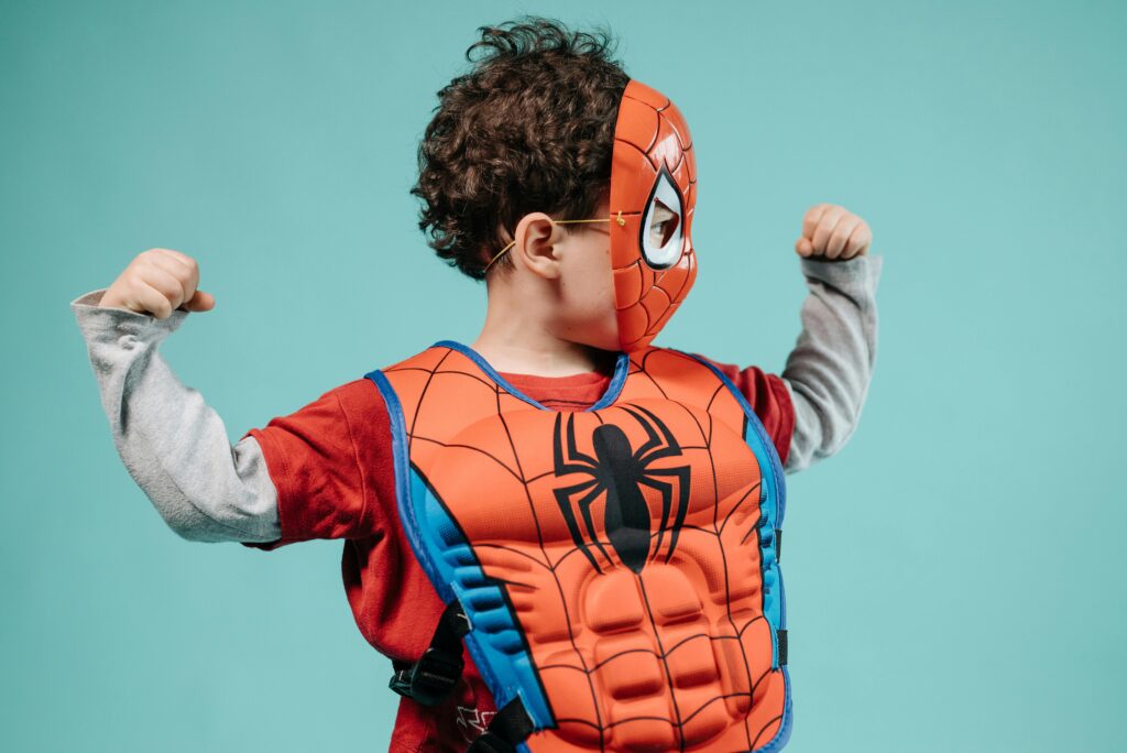 Young child posing in Spider-Man costume with turquoise background showcasing imagination.