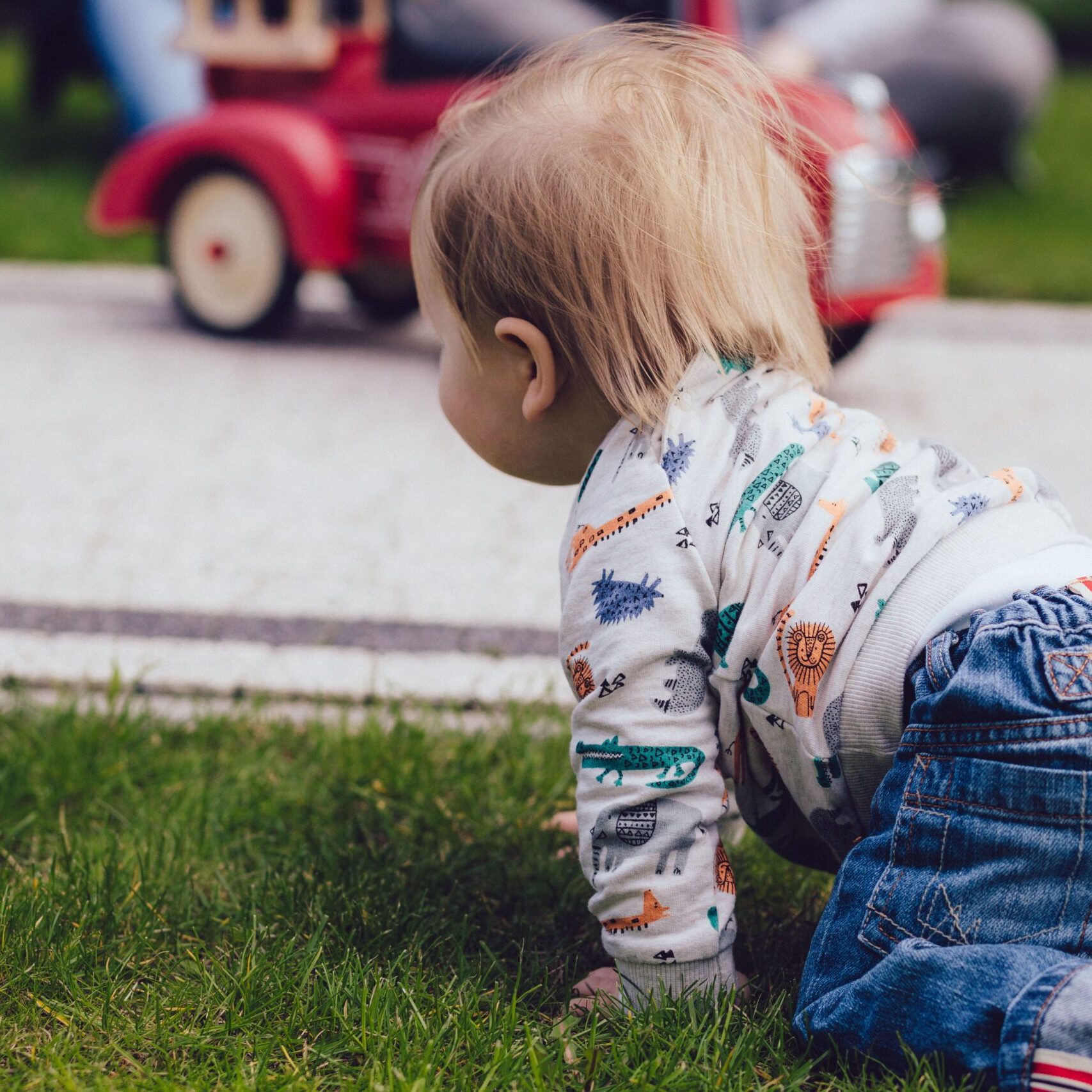 A toddler crawling on green grass outdoors near a toy car, enjoying a sunny day.