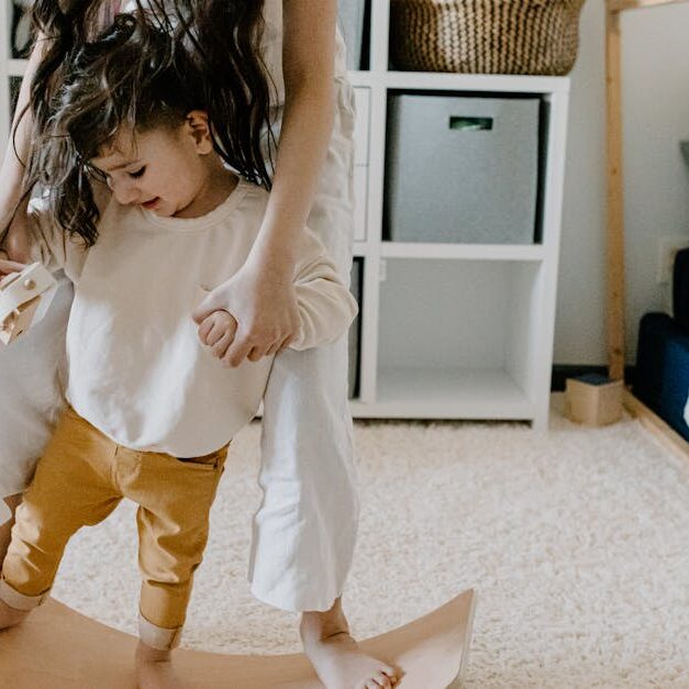 Mother and son enjoy bonding time in a cozy bedroom on a wooden balance board.