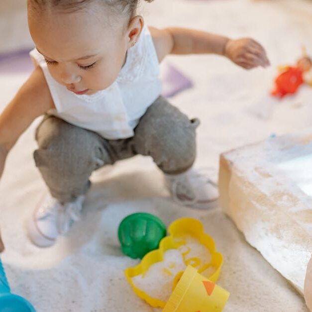 A toddler enjoys playing with colorful sand toys in an indoor play area, exploring and learning.